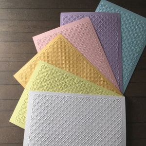 Può includere: Sei fogli di cartoncino testurizzato in vari colori pastello, tra cui azzurro, viola, rosa, giallo e verde. Il cartoncino presenta un motivo a rombi in rilievo.