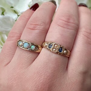 Op de afbeelding: Twee gouden ringen worden getoond, elk met een uniek ontwerp. E&eacute;n ring heeft drie opalen en kleine diamanten, de andere heeft afwisselend blauwe stenen en parels. De ringen staan tegen een neutrale achtergrond.