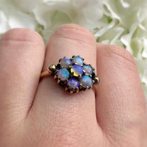 May include: A gold ring featuring a cluster of opals. The opals display a range of colors, including blue, purple, and yellow. The ring's band and setting are gold-toned, with a detailed design around each opal.