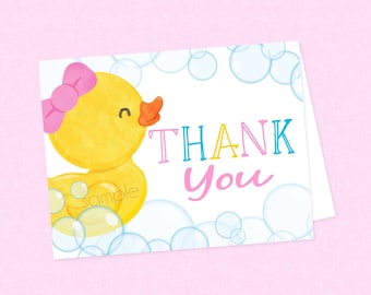 Könnte beinhalten: Eine gelbe Gummi-Ente mit einer rosa Schleife auf dem Kopf, umgeben von blauen und weißen Blasen. Der Text "THANK YOU" ist in bunten Buchstaben geschrieben.