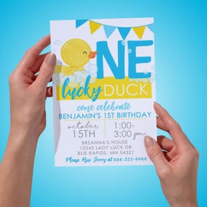 K&ouml;nnte beinhalten: Eine gelbe Gummi-Ente mit einem blauen und gelben Banner, auf dem "One Lucky Duck" steht, und einer blauen und gelben Einladung, auf der "Come Celebrate Benjamin's 1st Birthday" steht, mit Datum und Uhrzeit der Party.