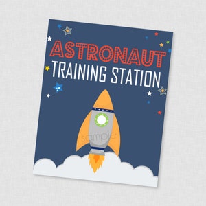 Puede incluir: Un cartel azul y blanco con el texto "Astronaut Training Station" en rojo. Un cohete de dibujos animados con llamas naranjas se lanza a una nube blanca sobre un fondo azul oscuro con estrellas blancas.