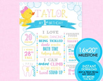 May include: A blue and pink printable milestone chart for a baby's first birthday. The chart features a cartoon rubber ducky, the name Taylor, and details about the baby's growth and development, including weight, height, and milestones like standing, waving, and blowing kisses. The chart is designed to be printed and displayed at the baby's first birthday party.