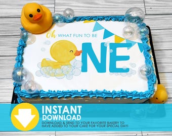 May include: A blue and yellow cake with a white frosting design featuring a rubber ducky, bubbles, and the text "Oh what fun to be ONE".