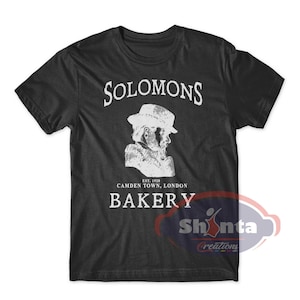May include: Black t-shirt with a white graphic design featuring a man with a beard and hat. The text reads "Solomons Bakery Est. 1920 Camden Town, London".