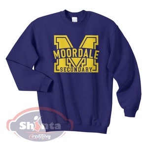 K&ouml;nnte beinhalten: Ein marineblauer Pullover mit einer gelben Grafik eines gro&szlig;en Buchstabens "M" mit dem Text "MOORDALE SECONDARY" im Buchstaben.