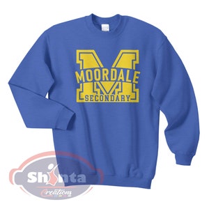 K&ouml;nnte beinhalten: Ein k&ouml;nigsblauer Pullover mit einer gelben Grafik eines gro&szlig;en Buchstabens "M" mit dem Text "MOORDALE SECONDARY" im Buchstaben.