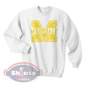 K&ouml;nnte beinhalten: Wei&szlig;er Pullover mit einem gelben Aufdruck eines gro&szlig;en Buchstabens M mit dem Text "MOORDALE SECONDARY" im Buchstaben.