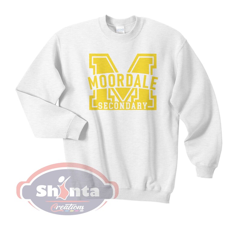 K&ouml;nnte beinhalten: Wei&szlig;er Pullover mit einem gelben Aufdruck eines gro&szlig;en Buchstabens M mit dem Text "MOORDALE SECONDARY" im Buchstaben.