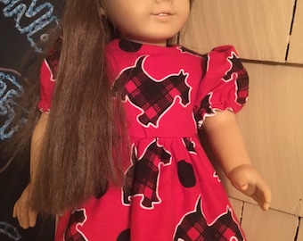 May include: A red dress with black and white plaid dogs and black polka dots. The dress has short sleeves with ruffles and a gathered skirt. The dress is made for a doll.