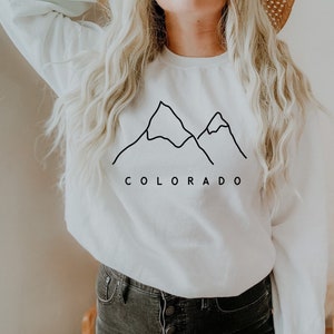 May include: White sweatshirt with a black outline of mountains and the word "COLORADO" printed on the front.