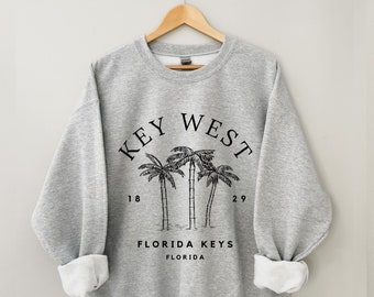 May include: Grey sweatshirt with a black graphic print of palm trees and the text "KEY WEST" in a circle. The text "FLORIDA KEYS" and "FLORIDA" are also printed below the circle.