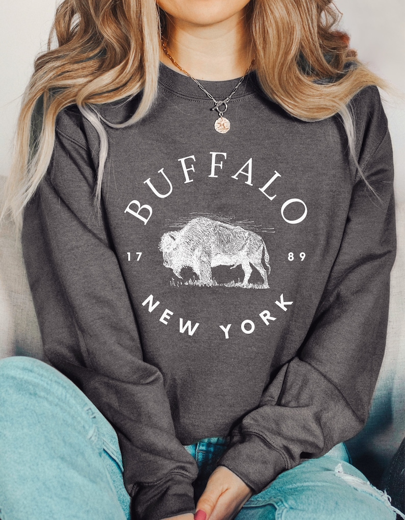 May include: A dark gray sweatshirt with a white graphic of a buffalo and the text "BUFFALO 1789 NEW YORK".