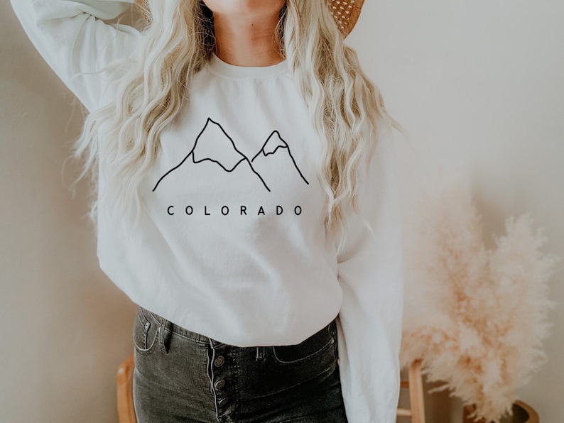May include: White sweatshirt with a black outline of mountains and the word "COLORADO" printed on the front.