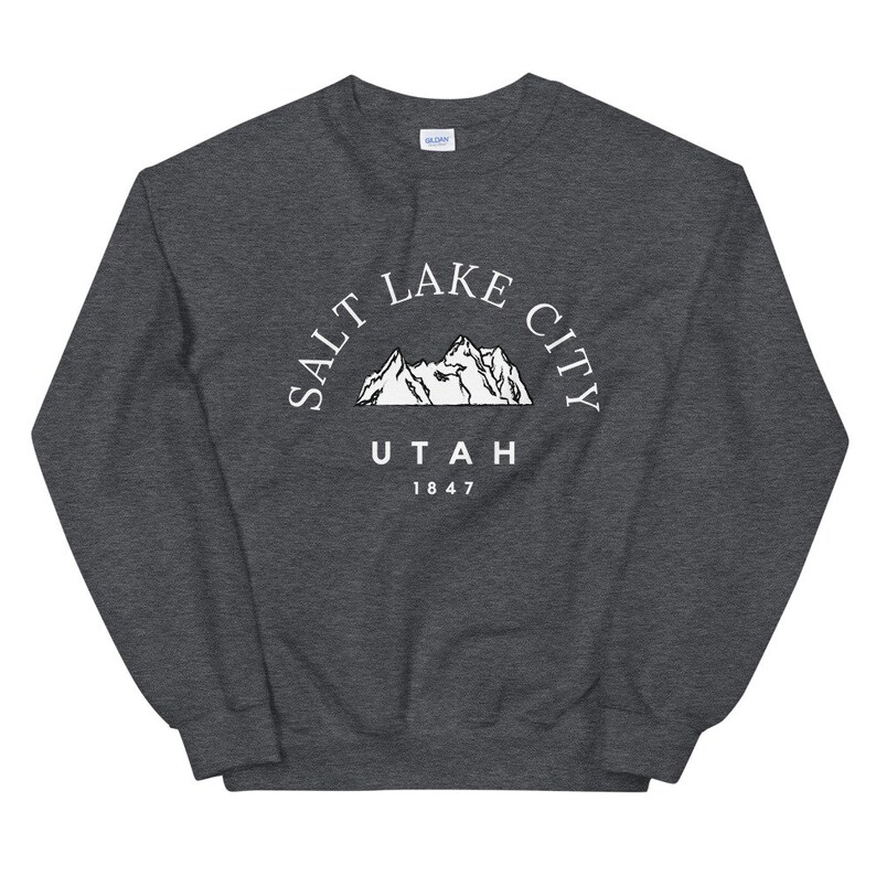 May include: Dark gray sweatshirt with the text "SALT LAKE CITY UTAH 1847" in white, arched above a mountain range graphic. The sweatshirt is a crew neck style.