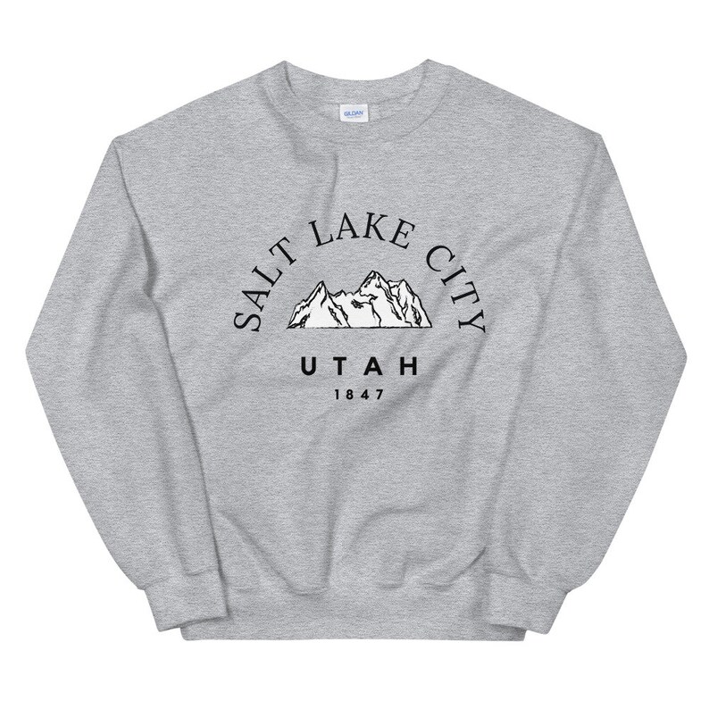 May include: A light gray sweatshirt with a crew neck. The front features a black graphic of mountains with the text "SALT LAKE CITY UTAH 1847" in a semi-circle above the mountains.