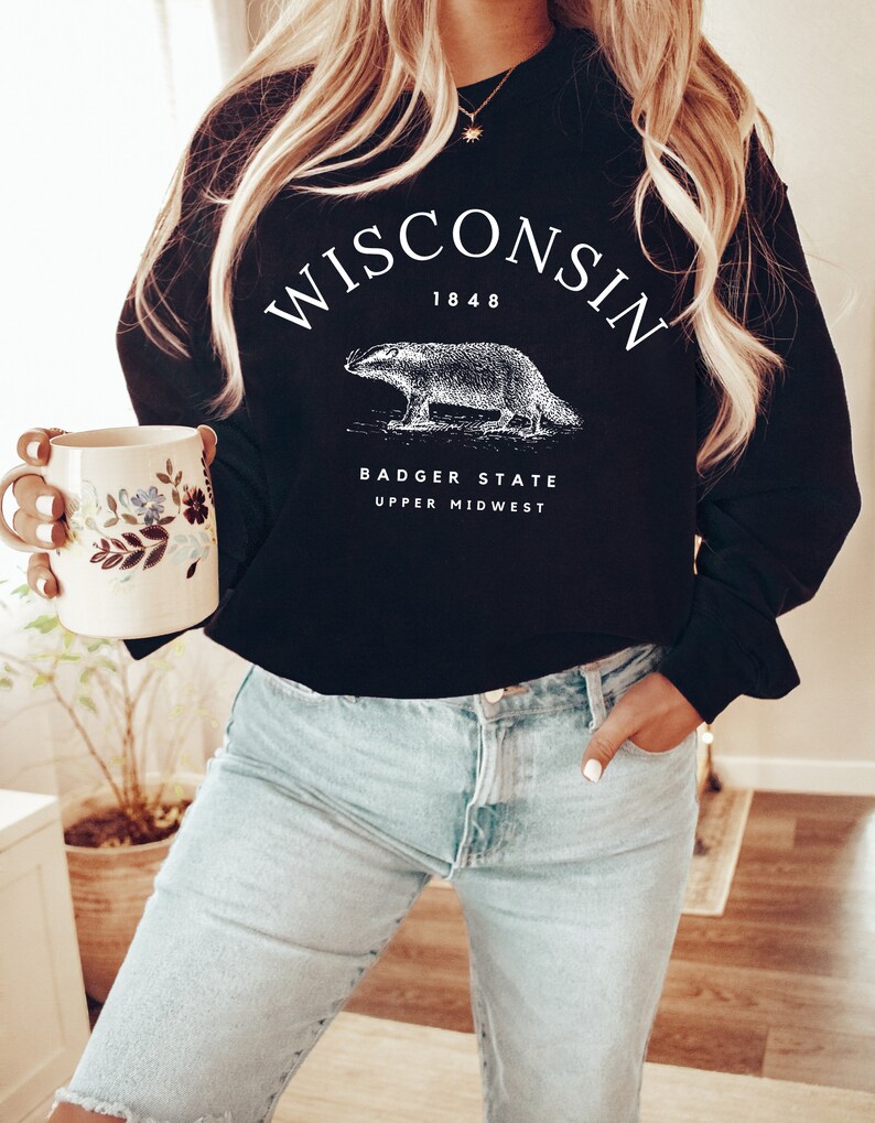 May include: Black sweatshirt with white text that reads "WISCONSIN 1848 BADGER STATE UPPER MIDWEST". A white illustration of a badger is centered on the sweatshirt.