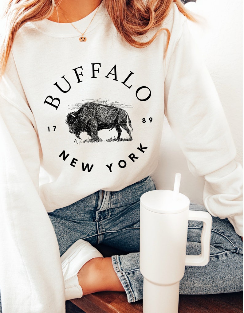 May include: White sweatshirt with a black graphic of a buffalo and the text "BUFFALO 1789 NEW YORK".