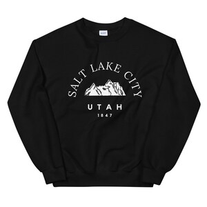 May include: Black sweatshirt with a white graphic of mountains and the text "SALT LAKE CITY UTAH 1847". The sweatshirt is made of a soft material and has a crew neck.