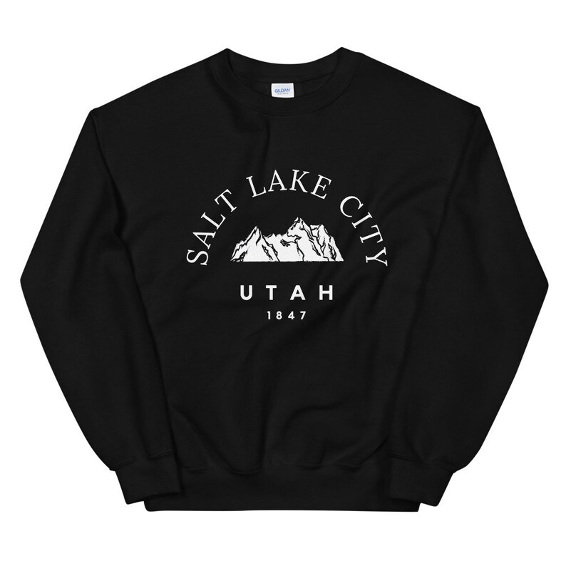 May include: Black sweatshirt with a white graphic of mountains and the text "SALT LAKE CITY UTAH 1847". The sweatshirt is made of a soft material and has a crew neck.