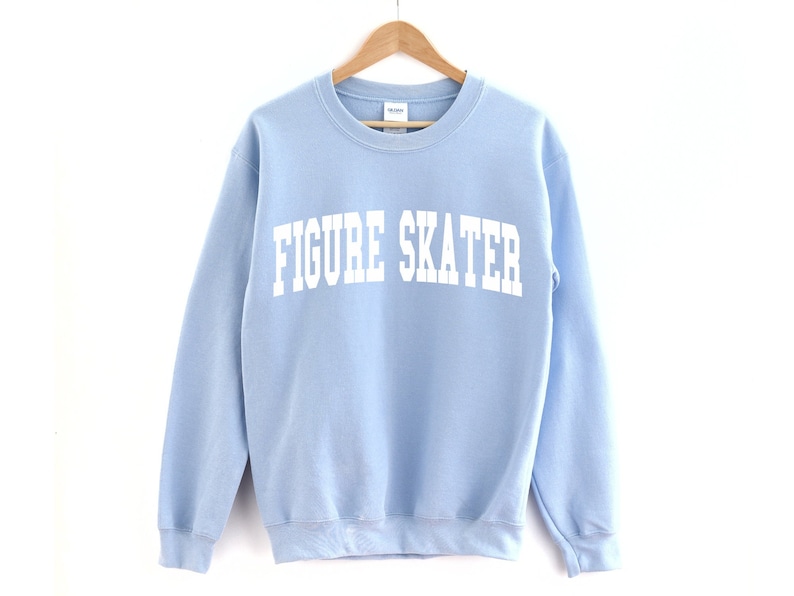 K&ouml;nnte beinhalten: Ein hellblauer Pullover mit dem Aufdruck "FIGURE SKATER" in Wei&szlig;.