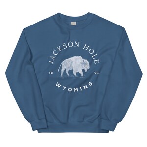 以下が含まれることがあります： 白い「Jackson Hole 1894 Wyoming」の文字が書かれた円の中に、白いバイソンのグラフィックが描かれた青いスウェットシャツです。