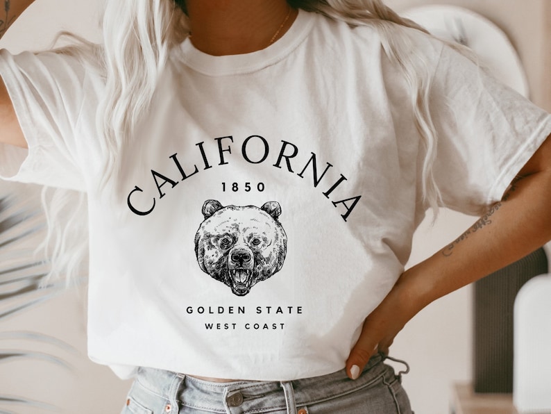 May include: White t-shirt with a black graphic design featuring a bear and the text "CALIFORNIA 1850 GOLDEN STATE WEST COAST".
