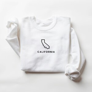 May include: White long-sleeved sweatshirt with a black outline of the state of California and the word "CALIFORNIA" printed below.