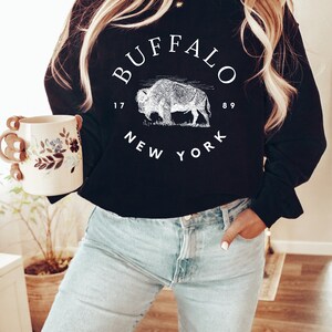May include: Black sweatshirt with a white graphic print of a buffalo and the text "BUFFALO 1789 NEW YORK".