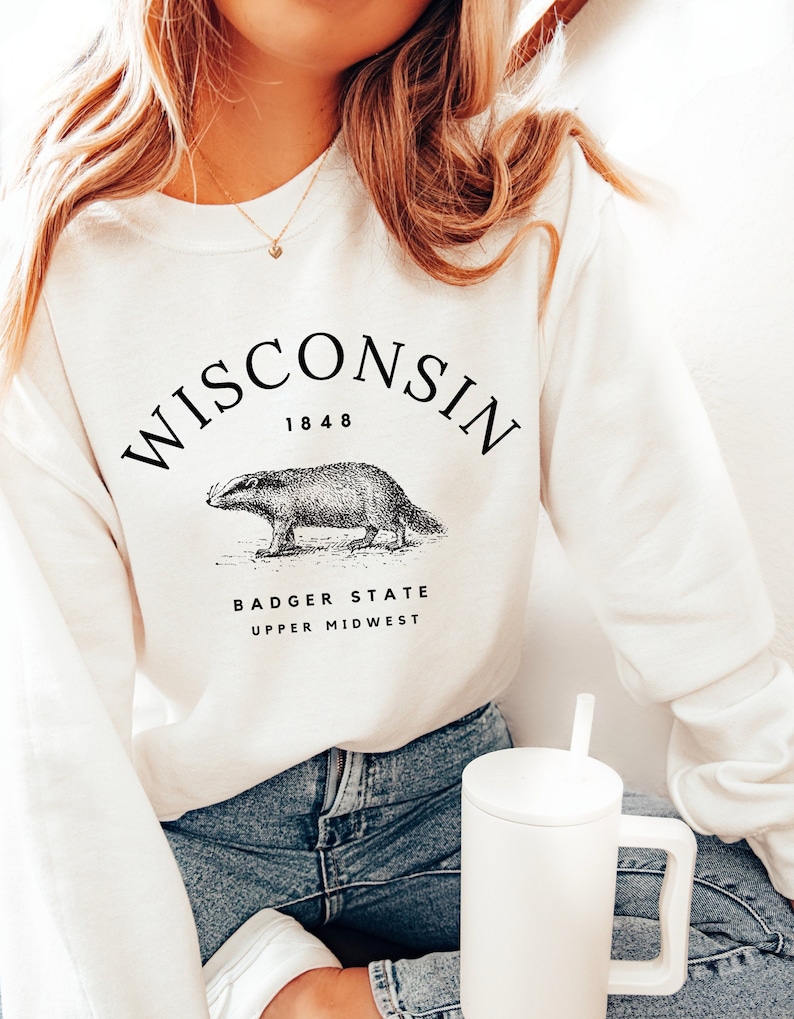 May include: White sweatshirt with a black graphic print of a badger and the text "WISCONSIN 1848 BADGER STATE UPPER MIDWEST".