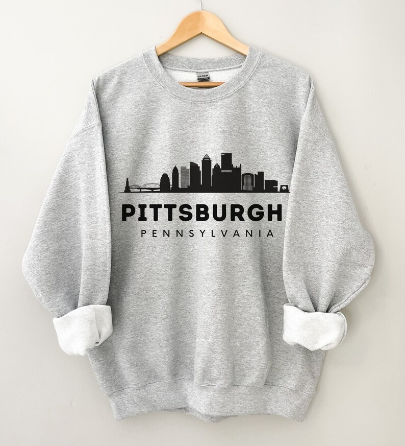 Może przedstawiać: Szara bluza z czarnym nadrukiem przedstawiającym panoramę Pittsburgha i tekstem "PITTSBURGH PENNSYLVANIA".