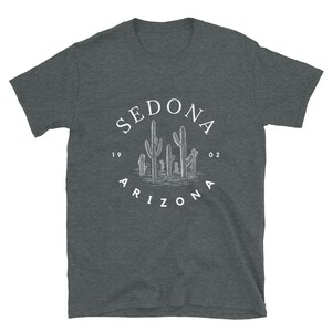 May include: A dark heather grey t-shirt with a white circle graphic featuring the text "SEDONA ARIZONA 1902" and a drawing of cacti.