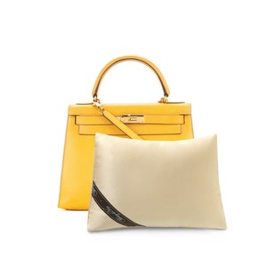 May include: A yellow leather handbag with gold hardware and a shoulder strap. The bag is sitting on a white dust bag with the text "Hermes Paris" printed on it.
