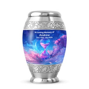 May include: A silver cremation urn with a decorative design. The urn features a blue and purple image of an hourglass against a cloudy sky. Text on the urn reads "In Loving Memory of Andrew Oct/1956-Jan/2026".