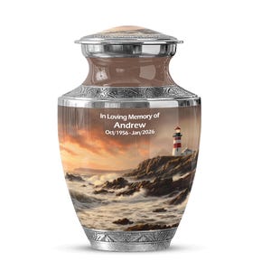 May include: A decorative urn with a lighthouse scene. The urn has a silver lid and base, with a brown and silver body. The text "In Loving Memory of Andrew Oct/1956-Jan/2026" is displayed on the front.