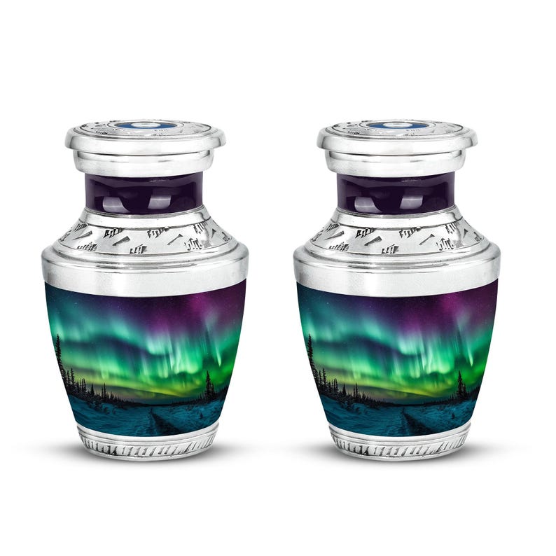 May include: Two silver-toned urns with a vibrant aurora borealis design. The urns feature a dark purple band and a detailed silver top. The base of each urn displays a landscape with green, purple, and blue hues, evoking a sense of the Northern Lights.