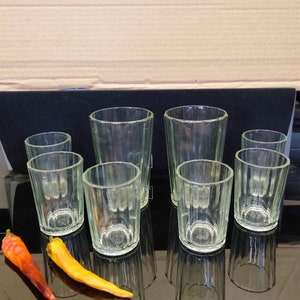 Puede incluir: Un juego de ocho vasos de chupito de vidrio transparente con un diseño acanalado. Los vasos están dispuestos en dos filas sobre una superficie negra. Un chile rojo y naranja está en primer plano.