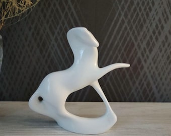 Puede incluir: Escultura de cerámica blanca de una liebre estilizada. La escultura tiene un acabado liso y brillante y un diseño minimalista. La liebre se representa en una pose dinámica, con las orejas y la cola extendidas.