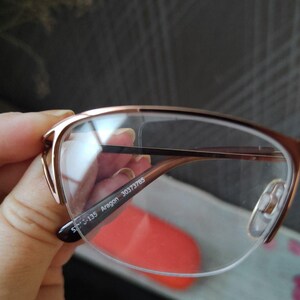 May include: Rose gold eyeglasses with a half-rim design. The glasses have clear lenses and a thin, delicate frame. The text "S-135 Aragon 30373785" is printed on the arm of the glasses.