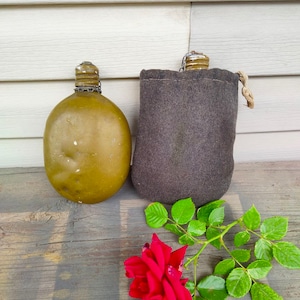 May include: Two olive green metal canteens with a brown fabric carrying case and a single red rose with green leaves on a wooden surface.