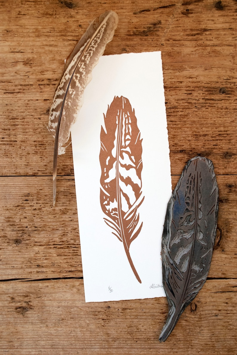 May include: A brown feather print on white paper with a woodblock carving of the same feather. The print is signed "Alethea".