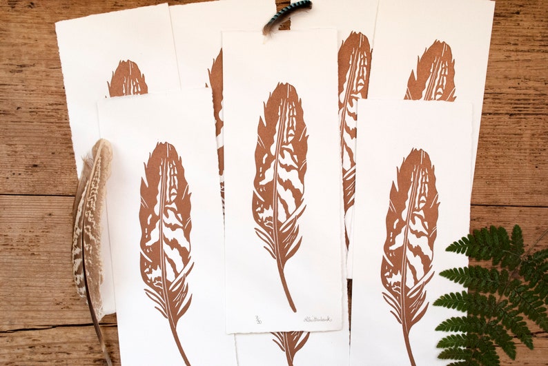 May include: Five brown prints of a single feather on white paper. The feather is detailed with a wood grain pattern. The prints are stacked on top of each other.