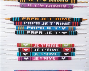 Op de afbeelding: Een verzameling kleurrijke vriendschapsarmbanden met verschillende zinnen zoals "MAMAN JE T'", "PAPA JE T'AIME", "JE T'AIME" en "TE QUIERO". Elke armband heeft een ander kleurenschema en een hartsymbool. De merknaam "Création INTIMIYUKI" staat bovenaan.