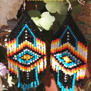 Peut inclure: Boucles d'oreilles perlées faites à la main avec un motif géométrique. Les boucles d'oreilles présentent des perles noires, turquoise, blanches, jaunes, oranges et rouges. Le texte "CREATION PACHAMAMA FAIT MAIN" est visible.