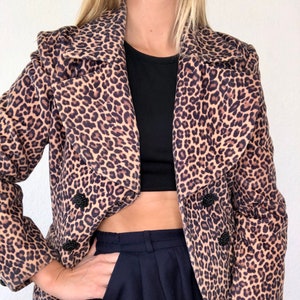 Könnte beinhalten: Ein brauner und schwarzer Leopardenmuster-Blazer mit doppelreihigem Verschluss und schwarzen Knöpfen. Der Blazer hat einen Schalkragen und lange Ärmel.