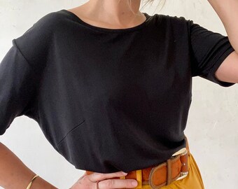 May include: A black short-sleeved t-shirt with a scoop neck and a brown leather belt with a decorative buckle. The belt is worn over a mustard yellow skirt.