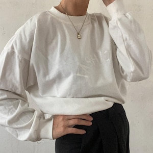 Op de afbeelding: Witte longsleeve trui met het woord "FASHION" geborduurd op de voorkant. De trui wordt gedragen met een zwarte rok.