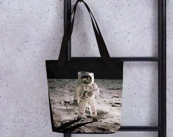 Może przedstawiać: Czarna torba typu tote z nadrukiem białego astronauty na Księżycu.