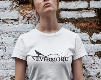 Puede incluir: Camiseta blanca con una silueta negra de un cuervo posado en una rama con el texto "NEVERMORE" debajo.