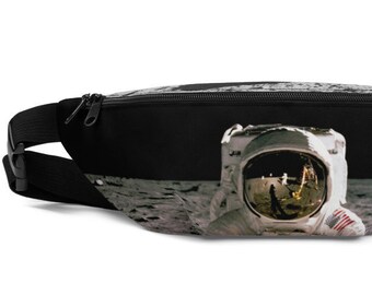 Może przedstawiać: Czarna nerka z zamkiem błyskawicznym i regulowanym paskiem. Przód nerki przedstawia zdjęcie astronauty na Księżycu.